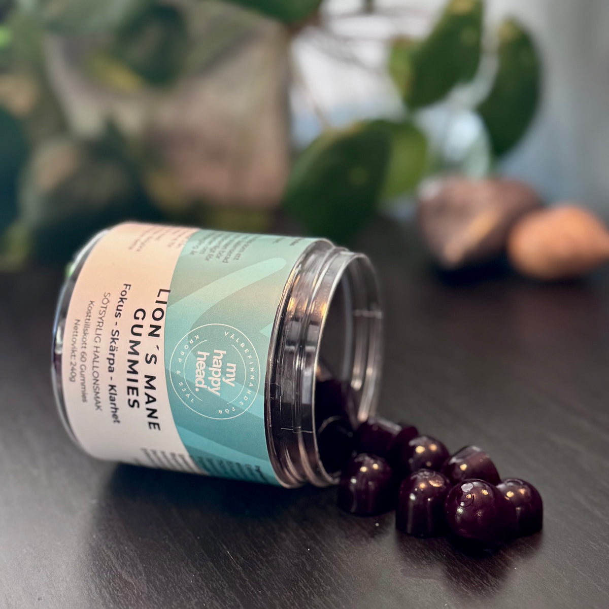 Öppen burk med Lion’s Mane Gummies från My Happy Head, några mörklila gummies ligger utspillda på ett mörkt bord.