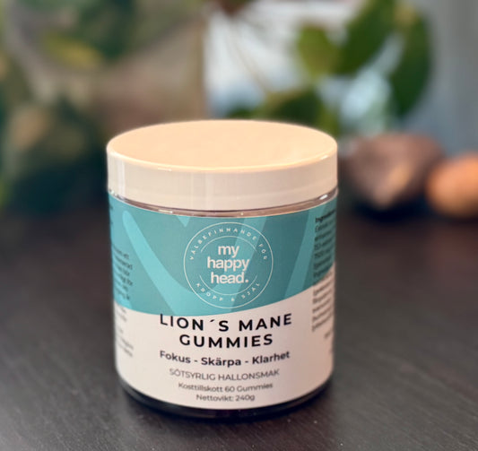 Burk med Lion’s Mane Gummies från My Happy Head på mörkt bord, med gröna blad i bakgrunden.