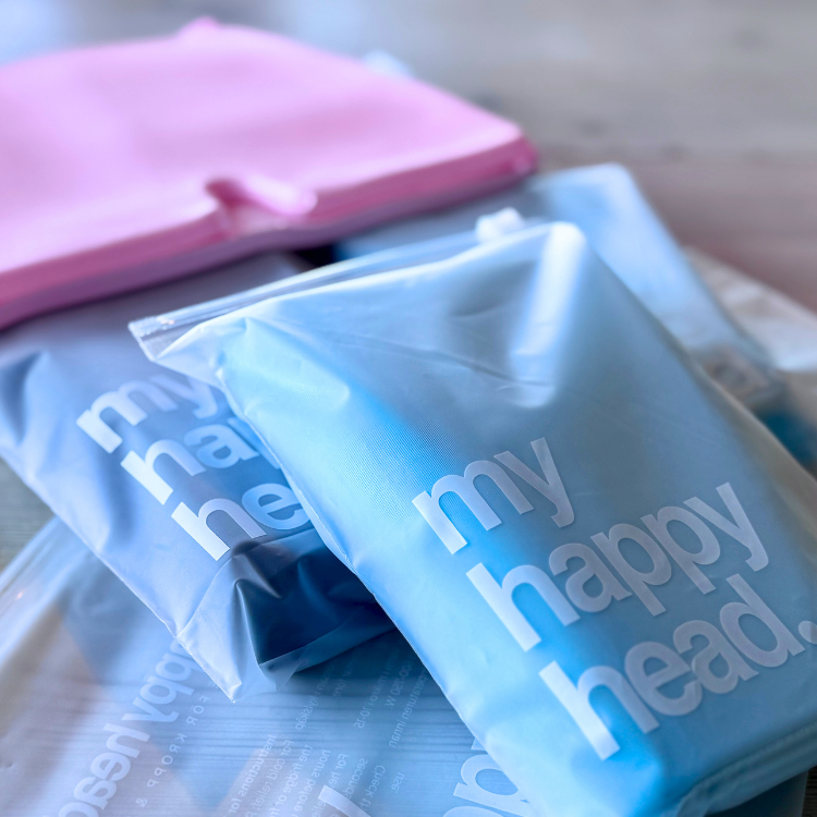 Huvudvärksmössor från My Happy Head i blå, svart och rosa förpackningar, redo för leverans.